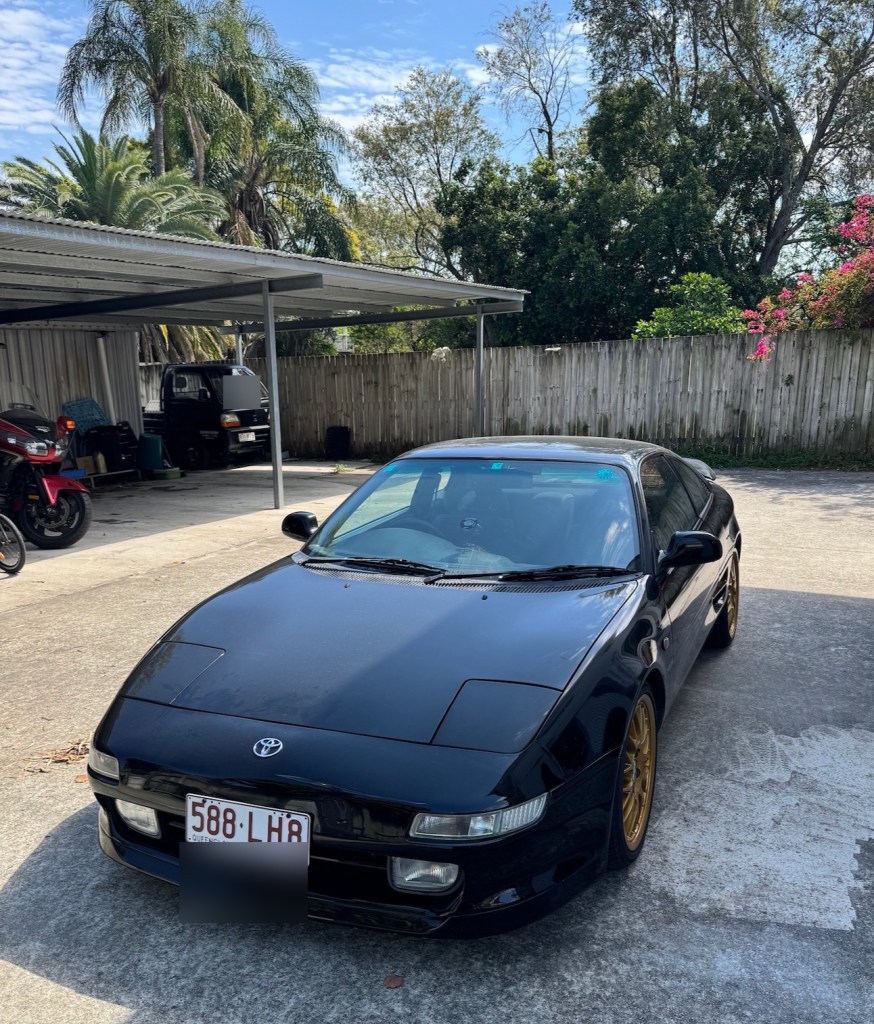 Black 1997 Toyota MR2 with its pop-up headlights closed; number plates blurred.